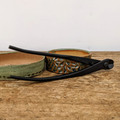 A pair of professional Tinyroots black carbon steel concave branch cutters rests across two handcrafted ceramic bonsai pots on a weathered wooden surface. The pot on the left is a shallow, round dish with a speckled sage green glaze and a natural tan interior. Beside it, the second pot features a heavily textured, carved exterior with green and brown glazes. The matte black bonsai tool, with the "Tinyroots" brand name visible on the handle, is part of a high-quality carbon steel tool kit designed for precise bonsai maintenance. The background is a clean, minimalist off-white, emphasizing the artistic and functional nature of the bonsai starter kit items.