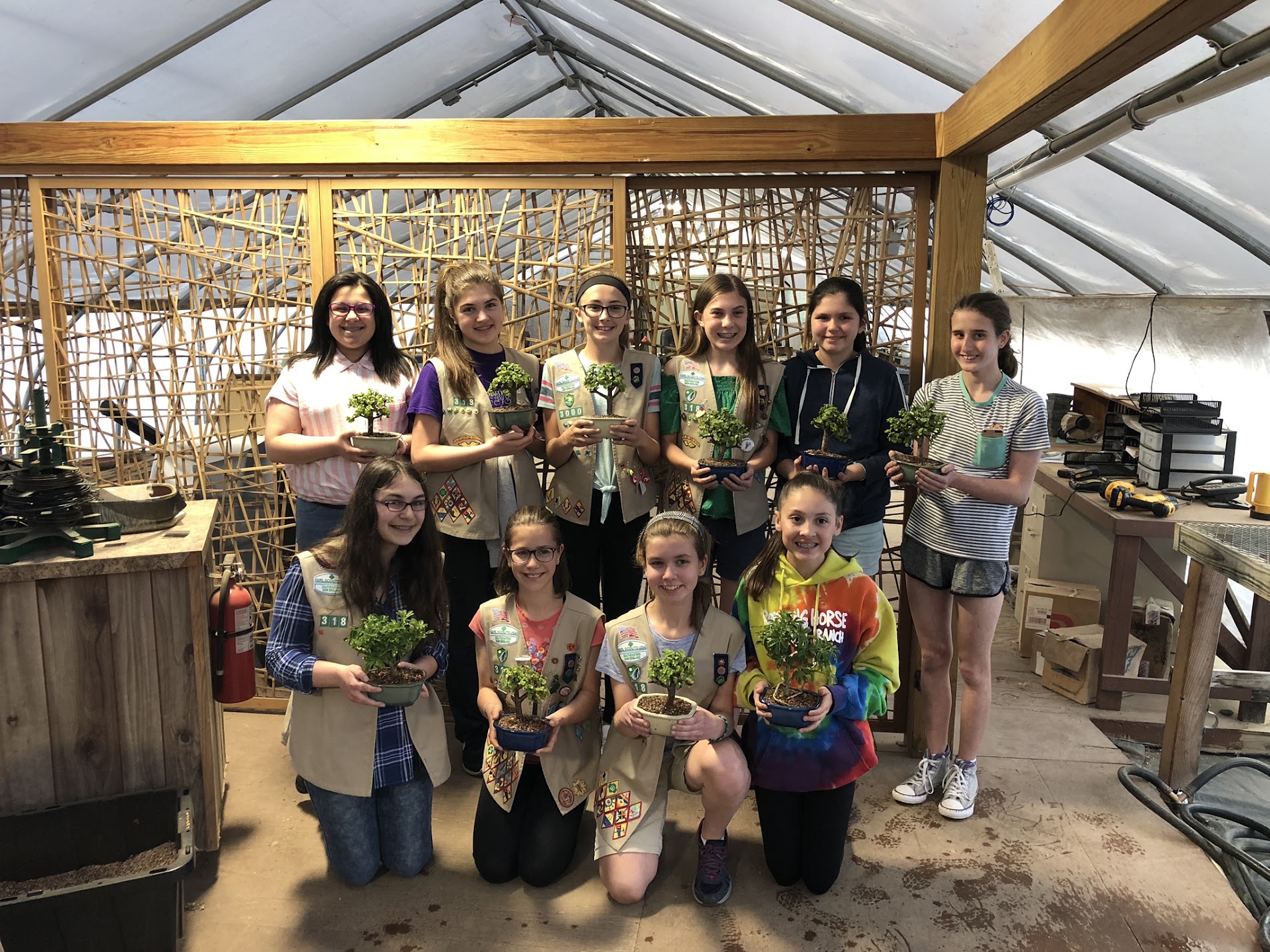 A scout troop in the greenhouse holding the bonsai trees they styled