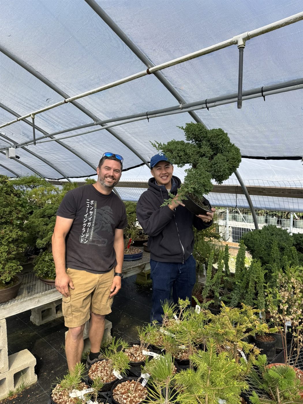 Peter Olson in the greenhouse with a student holding a shimpaku juniper