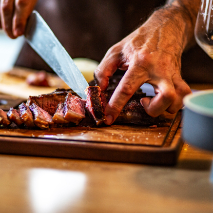 Closeup of man cutting into a premium steak with a kitchen knife.