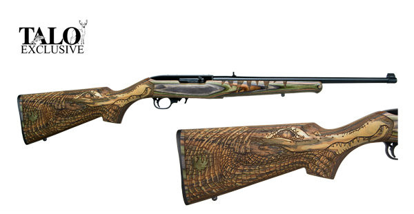 Ruger 10/22 .22 lr (38.5" long with 20" barrel). The barrel is finished in a matte black and is equipped with a folding leaf rear sight and a gold bead front sight. This 10/22 is a special TALO edition with a Green Mountain Gator engraved on the stock.
