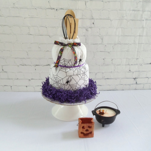 Kitchen towel cake with purple shred, a spider web kitchen towel, and a variety of utensils sticking out the top.
