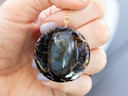 In-hand shot: "Gold-filled botanical pendant with a Labradorite gemstone and black tea leaves in natural light."