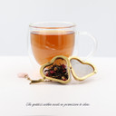 Cup of brewed Goddess Grey black tea with a gold heart-shaped tea infuser filled with loose-leaf tea.
