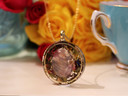Side view of round Rose Quartz and White Tea pendant showing the dimensional stone, botanical layers and gold-tone frame.