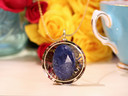 Front view of The Scribe pendant featuring large AAA Sodalite surrounded by White Tea, colorful botanicals and gold details
