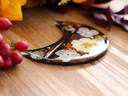 Close side view of handmade botanical tarot card holder with cream and lavender pressed flowers, orange foliage and gold leaf in dark resin.