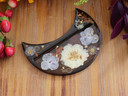 Top view of crescent-shaped botanical tarot card holder with cream and lavender flowers, orange foliage and gold leaf in dark resin.