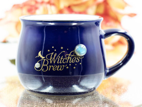 Royal blue ceramic cauldron mug with matte gold "Witches Brew" design, black rim, white interior, and two Labradorite gemstones, front view on white background. Royal blue ceramic cauldron mug with matte gold "Witches Brew" design, black rim, white interior, and two Labradorite gemstones, front view on white background.