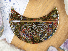 Crescent moon stand with green tea, saffron, and cornflower petals encased in resin, featuring a delicate engraved butterfly design. Crescent moon stand with green tea, saffron, and cornflower petals encased in resin, featuring a delicate engraved butterfly design.