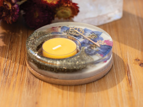 A handcrafted resin candle holder with pressed blue and pink blossoms, golden key, and pyrite dust, holding a beeswax tealight, displayed on a wooden table. A handcrafted resin candle holder with pressed blue and pink blossoms, golden key, and pyrite dust, holding a beeswax tealight, displayed on a wooden table.