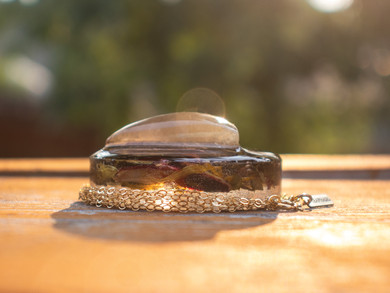 Profile view of a handcrafted 14k gold-filled round pendant infused with a triangle golden rutile quartz stone, green tea, and hibiscus herbs in eco resin. Hanging from a 16" 14k gold-filled chain.