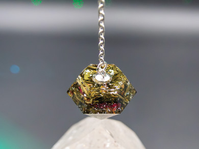 Close-up of Radiant Soul pendulum showing green tea leaves, rose petals, and silver flecks inside resin.