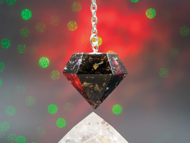 Close-up of Oracle Moon pendulum showing layers of black tea leaves, rose petals, blue cornflower, lemongrass, and metallic flecks sealed in resin.