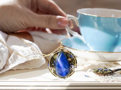 I OWN MY TRUTH pendant featuring a AAA Lapis Lazuli set in green tea leaves with a gold inset ring. Hand holding a teacup in the background.