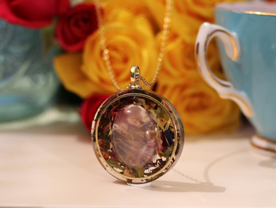 Side view of round Rose Quartz and White Tea pendant showing the dimensional stone, botanical layers and gold-tone frame.