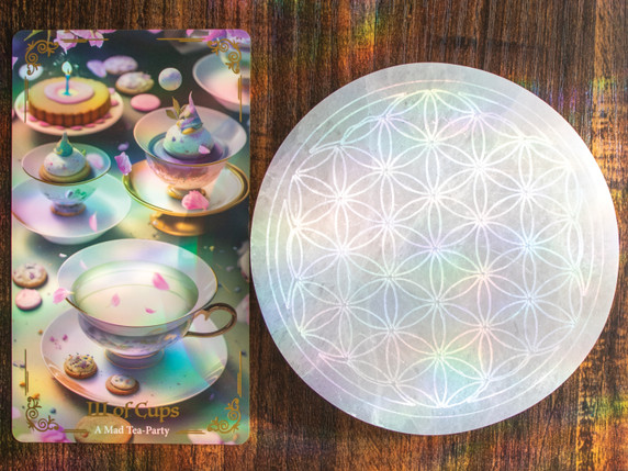 Flower of Life selenite charging plate laying next to a tarot card, highlighting its use for cleansing and charging.