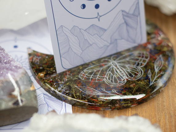 Butterfly engraving and vibrant botanicals frame the card, glowing under the resin’s glass-like finish.