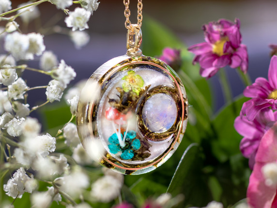 Side View. Flower Moon, Version A. Handcrafted crescent moon featuring mini blossoms, green tea, and blue flash moonstone lying on a bed of green tea leaves.