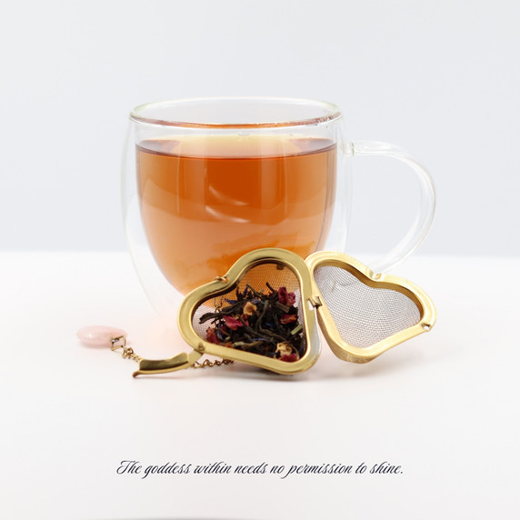 Cup of brewed Goddess Grey black tea with a gold heart-shaped tea infuser filled with loose-leaf tea.