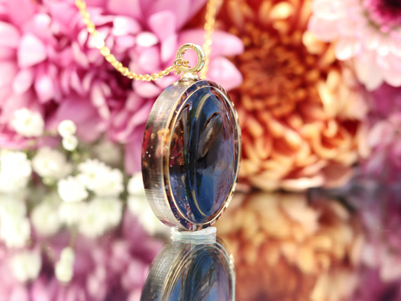 Side view of a Hypersthene tea-infused pendant showing the gemstone, botanical resin setting and gold frame.