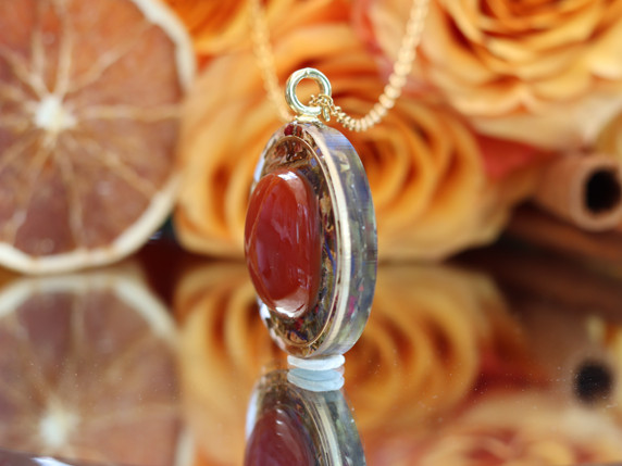 Side profile of the Life Force Energy tea-infused pendant showing the raised Carnelian stone and dimensional clear resin design.
