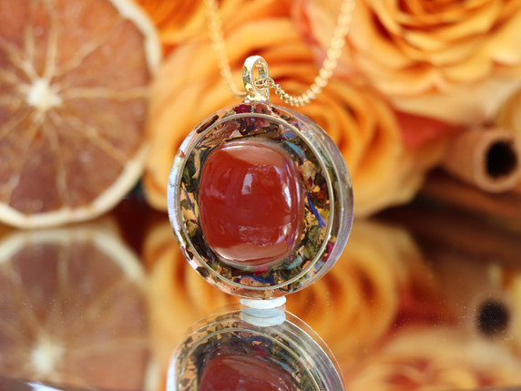 Life Force Energy Carnelian pendant shown from a slight angle, highlighting the gemstone, tea botanicals and gold-tone setting.