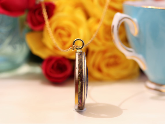 Close angled view of The Scribe tea-infused pendant featuring AAA Sodalite in a round gold-tone frame