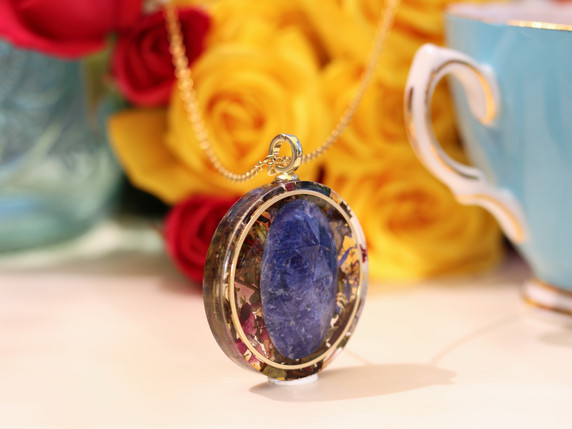 Side view of The Scribe tea-infused pendant showing layered White Tea botanicals, gold-tone frame and faceted Sodalite