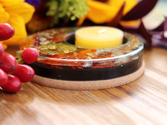 Close side view of handmade resin candle holder showing layered pressed autumn flowers, metallic leaf, Shungite and natural cork base.