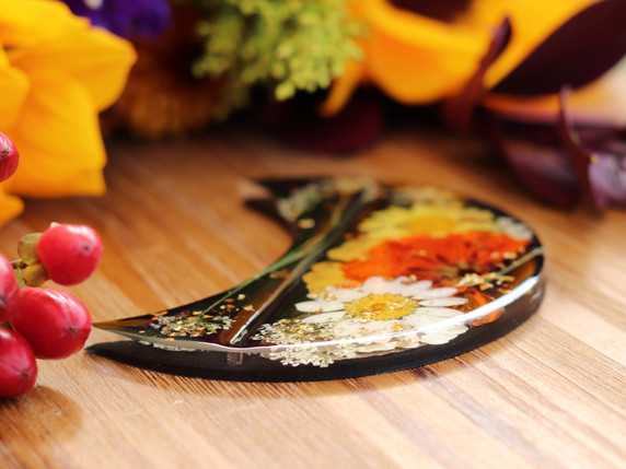Low-angle view of botanical resin tarot card holder showing layered pressed flowers, metallic leaf and glossy black edges.