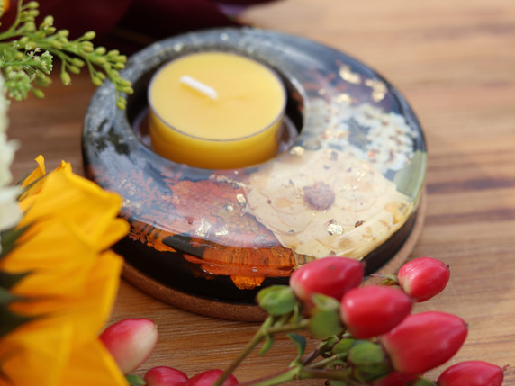 Close angled view of handmade candle holder featuring cream blossoms, orange botanicals and metallic leaf suspended in dark resin.