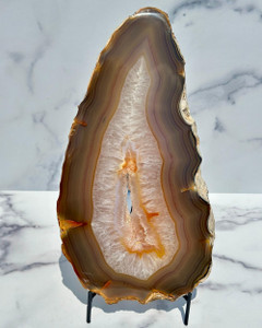 Banded gray agate slab with quartz druzy center, front polished, upright on a black metal stand against white marble