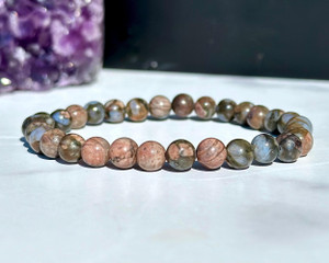Que Sera elastic bracelet with 6mm pink, blue and olive mottled beads displayed beside a purple amethyst cluster