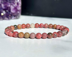 Rhodonite elastic bracelet with 6mm pink and gray beads displayed beside a purple amethyst cluster
