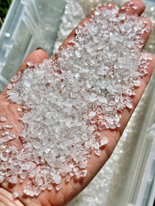 Handful of clear quartz crystal chips 3mm to 5mm Grade AB held over a bin of bulk quartz chips