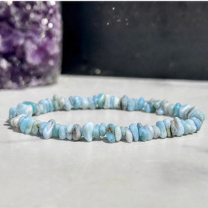 Larimar chip bead elastic bracelet on a white marble surface with an amethyst cluster in the background