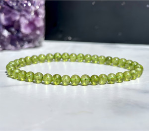 Peridot Elastic Bracelet with 4mm beads on white marble beside an amethyst cluster