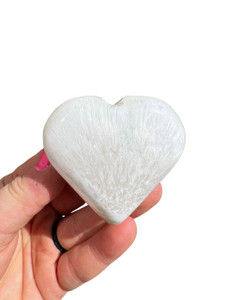 Polished white Scolecite heart held in hand, showing fine radiating needle-like crystal fibers