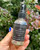Hand holding the Cinnamon Crystal Spray bottle among green leaves and orange flowers