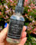 Hand holding the Cinnamon Crystal Spray bottle in front of blooming pink flowers