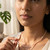 Woman wearing a faceted pink opal necklace layered with a pendant near greenery