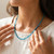 Woman wearing a faceted blue apatite necklace with her hands near her collarbone