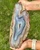 Blue banded agate slab held upright outdoors, showing the full teardrop shape and raw tan edge