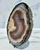 Banded agate slab angled on its stand, showing the sparkling dark druzy crust along the outer edge