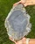 Hands holding the unpolished gray back of the large agate slab outdoors over green grass