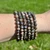 Stack of Que Sera 6mm elastic bracelets worn on a wrist outdoors above green grass