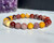 Mookaite elastic bracelet with 8mm mustard yellow, deep red, and cream beads resting beside a purple amethyst cluster