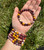 Open palm holding a Mookaite elastic bracelet with four more stacked on the wrist outdoors