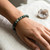 Seraphinite bracelet worn on a wrist on white linen beside a small geode